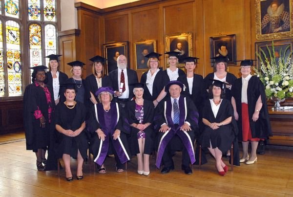 IAM graduates in gowns and mortarboards with officers in ceremonial robes in a panelled hall with stained glass