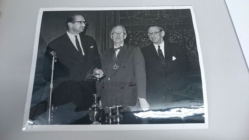 Archive photograph of three Institute officers standing at a microphone, one wearing the presidential chain of office